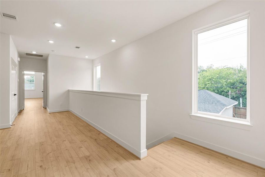 Upper-level landing — bright picture window framing tree-lined views, half-wall partition, and wide-plank wood-look flooring throughout.