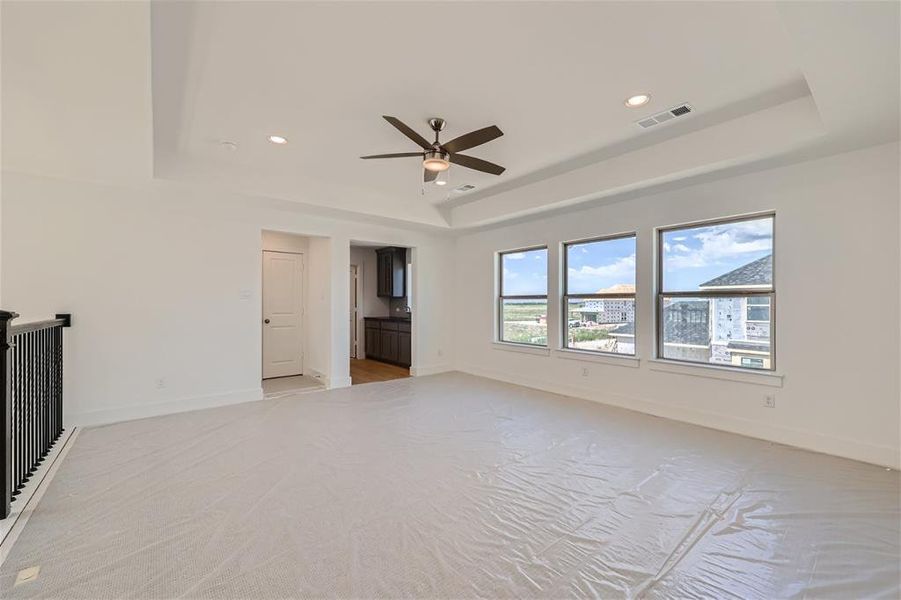 Unfurnished living room featuring a raised ceiling, light colored carpet, and ceiling fan