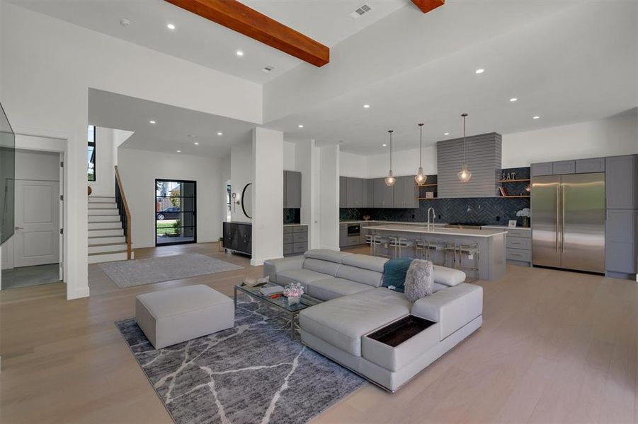 Living room featuring a towering ceiling, beam ceiling, sink, and light hardwood / wood-style flooring