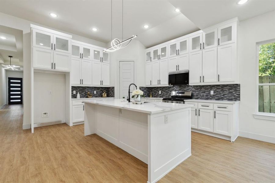 Kitchen featuring backsplash, light hardwood / wood-style flooring, appliances with stainless steel finishes, sink, and a center island with sink