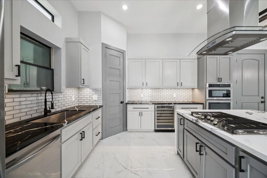 Sophisticated design meets functionality in the kitchen, featuring a spacious island with gas cooktop, sleek cabinetry, and a mix of light and dark finishes. Stainless steel appliances, a wine cooler, and double ovens make meal preparation effortless, while the backsplash and modern hardware add refined detail.