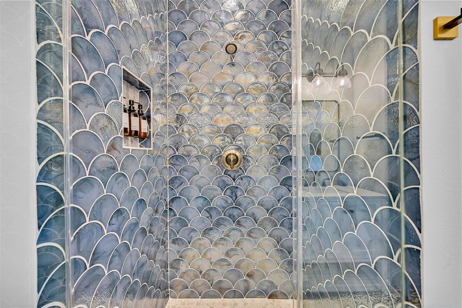 The enclosed shower instantly becomes a showpiece with striking mermaid inspired tile work that adds texture, movement, and coastal personality to the space.