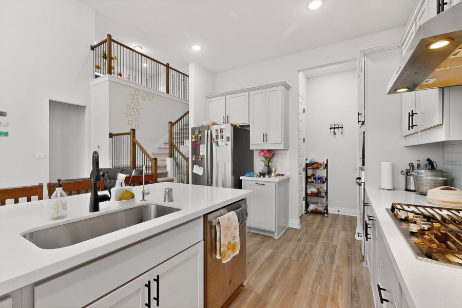 Kitchen with white cabinets, under cabinet range hood, light wood-type flooring, appliances with stainless steel finishes, and decorative backsplash