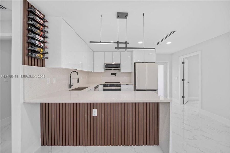 Modern kitchen featuring white cabinetry, light-colored countertops, stainless steel appliances, and wood-finish paneling on the kitchen island Modern kitchen featuring white cabinetry, light-colored countertops, stainless steel appliances, and wood-finish paneling on the kitchen island