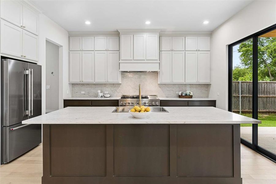 Kitchen featuring a large island with an integrated sink, white extended upper cabinetry, dark lower cabinetry, stainless steel appliances, and a full nine foot height sliding glass door. Kitchen featuring a large island with an integrated sink, white extended upper cabinetry, dark lower cabinetry, stainless steel appliances, and a full nine foot height sliding glass door.