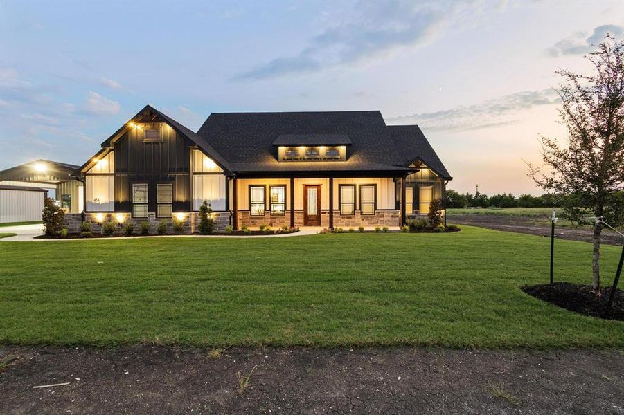 Modern inspired farmhouse with a porch, board and batten siding, a front lawn, roof with shingles, and stone siding