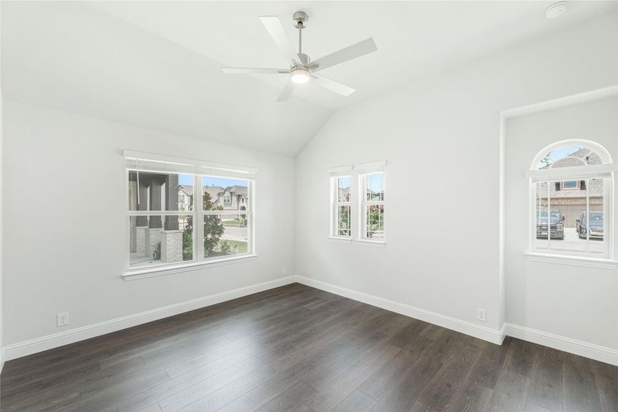 Empty bedroom with vaulted ceiling, ceiling fan, dark hardwood floors, and multiple windows Empty bedroom with vaulted ceiling, ceiling fan, dark hardwood floors, and multiple windows