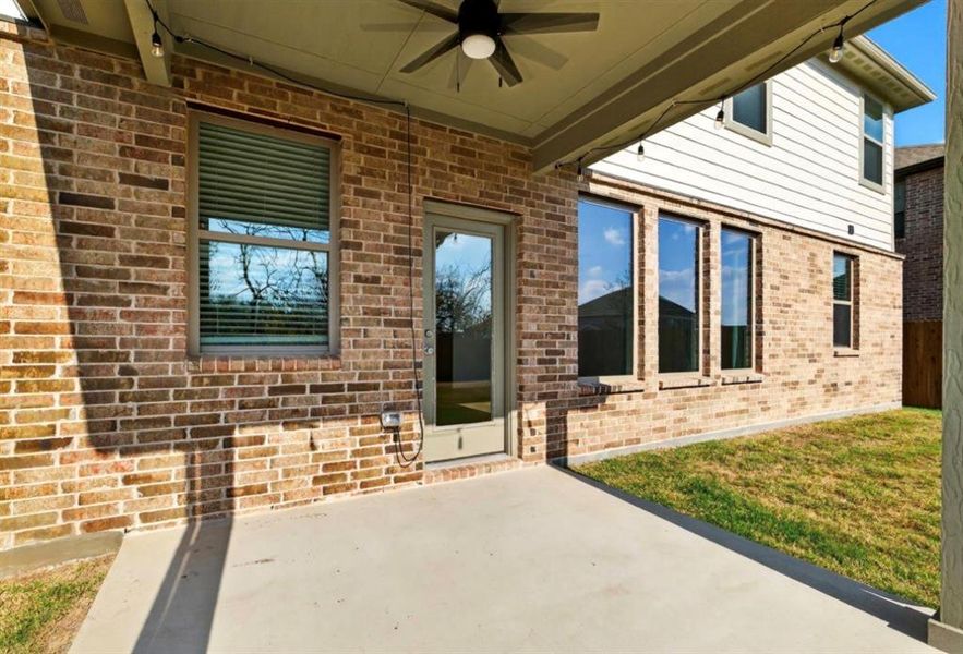 Doorway to property with brick siding, a ceiling fan, a patio, and a lawn