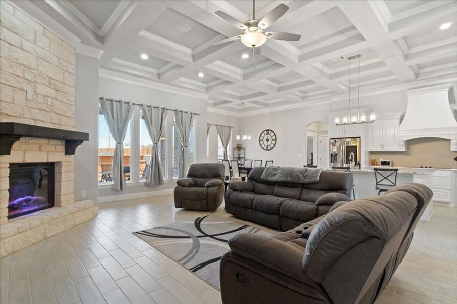 Living room with light wood-style floors, beam ceiling, a stone fireplace, and a towering ceiling