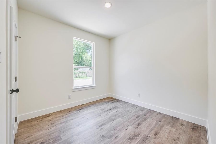 Room featuring wood-finish flooring, recessed ceiling light, white baseboards, and a window with a white frame Room featuring wood-finish flooring, recessed ceiling light, white baseboards, and a window with a white frame
