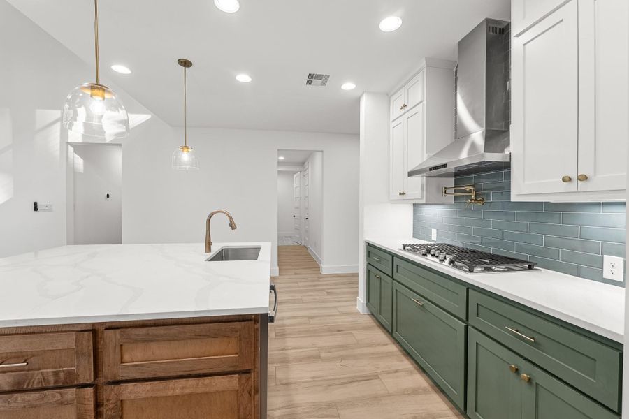 This modern kitchen features a sleek design with a large white quartz island, pendant lighting, and wood accents. The space includes a stylish backsplash, stainless steel hood, and green lower cabinets, creating a fresh, inviting atmosphere. This modern kitchen features a sleek design with a large white quartz island, pendant lighting, and wood accents. The space includes a stylish backsplash, stainless steel hood, and green lower cabinets, creating a fresh, inviting atmosphere.