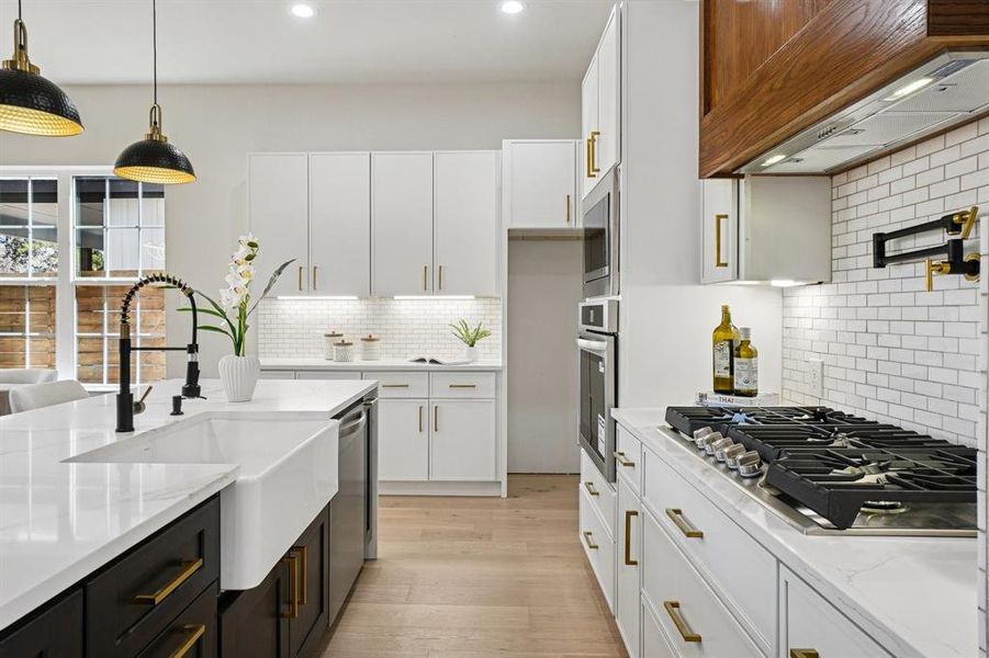Kitchen featuring two tone cabinetry, light stone countertops, pendant lighting, stainless steel appliances, and light wood-type flooring