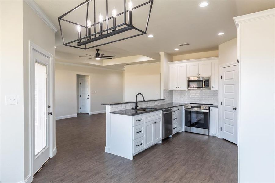 Kitchen featuring white shaker cabinetry, dark countertops, stainless steel appliances, and a subway tile backsplash