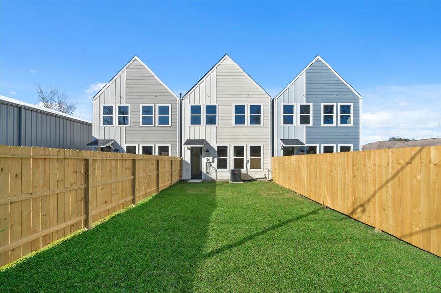 This photo shows a modern townhouse with three distinct sections, featuring a symmetrical design and large windows. It's surrounded by a wooden fence and has a well-maintained grassy yard, offering privacy and outdoor space.