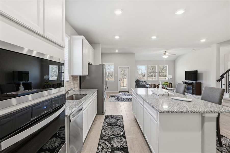 Kitchen featuring white cabinetry, stainless steel appliances, light-toned wood-finish flooring, a light-toned granite island, and recessed lighting