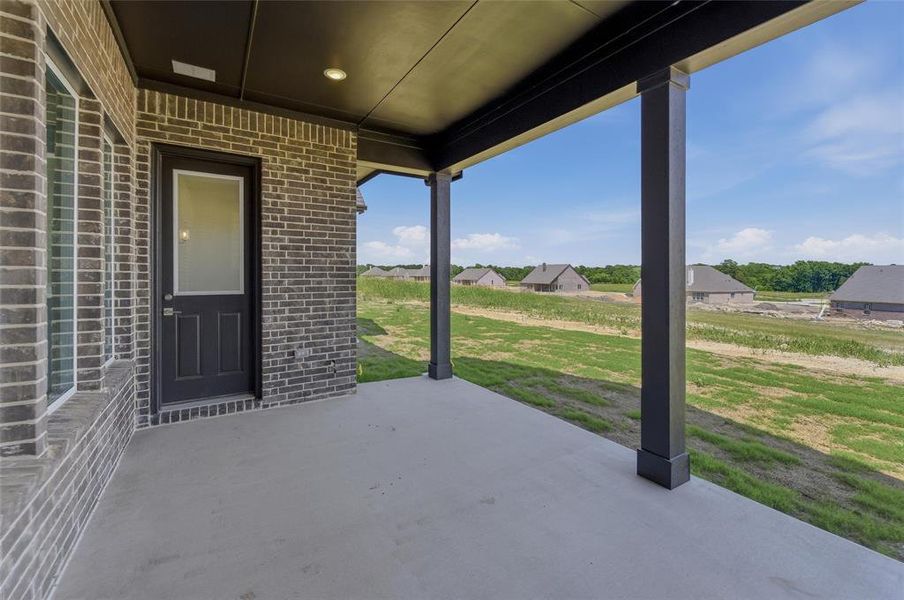 Covered patio featuring a concrete surface, dark brick exterior, recessed lighting, and a dark-paneled door with an upper glass pane