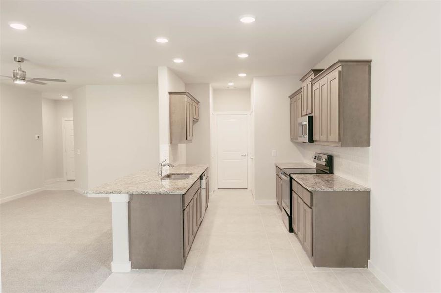 Kitchen with appliances with stainless steel finishes, light stone counters, backsplash, light carpet, and ceiling fan