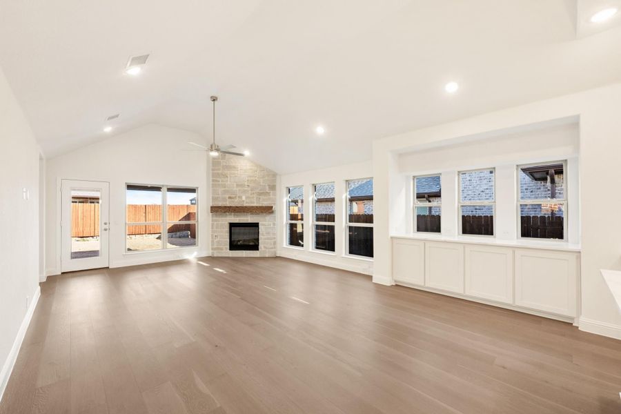 Open living room with vaulted ceiling, stone fireplace, hardwood floors, and large windows Open living room with vaulted ceiling, stone fireplace, hardwood floors, and large windows