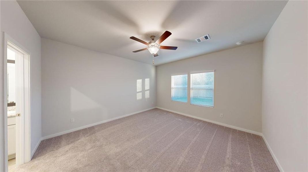 This spacious bedroom features neutral carpeting and paint, a ceiling fan, and two large windows that let in natural light. There's an adjoining bathroom for added convenience.