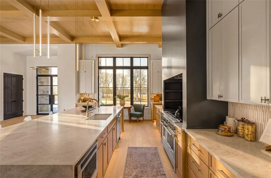 Spacious kitchen featuring a large central island with an integrated sink, light-toned countertops, wood-finish flooring, and a coffered ceiling