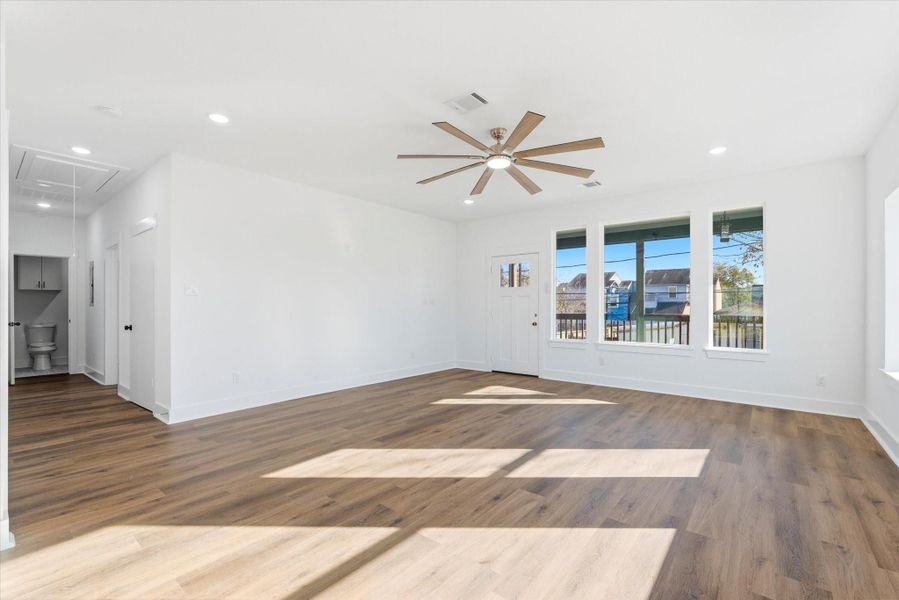 Step into a light-filled, spacious living room enhanced by an oversized ceiling fan, recessed lighting, and beautiful picture windows.