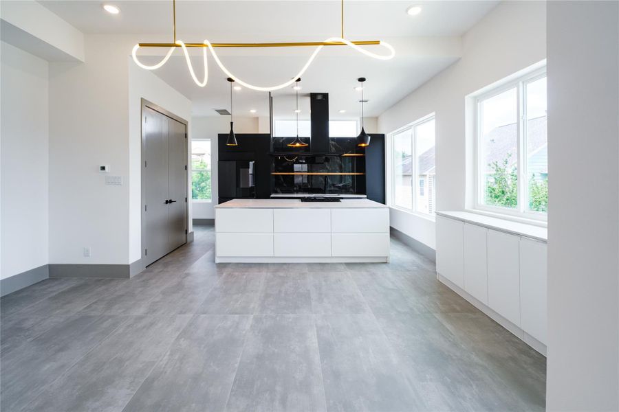 Representative Middle Level Kitchen/Dining/Living View (Design selections and colors may vary): The open -plan middle level seamlessly integrates the kitchen, dining and living spaces, perfect for both daily living and entertaining.  Large cement-like gray tiles flooring and added quartz counter/cabinet storage space by window near dining are some of the select upgrades incorporated into a different unit.