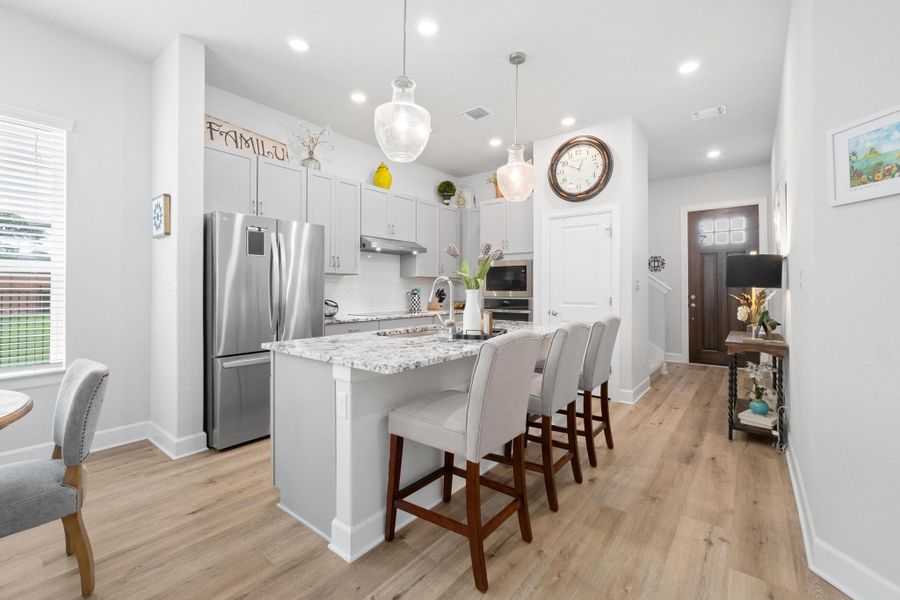 Kitchen featuring decorative backsplash, a kitchen island with sink, under cabinet range hood, a breakfast bar, and stainless steel appliances Kitchen featuring decorative backsplash, a kitchen island with sink, under cabinet range hood, a breakfast bar, and stainless steel appliances