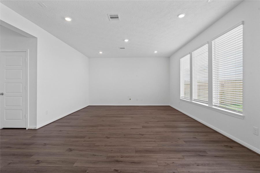 Bring family and friends together in this beautiful family room! It features high ceilings, recessed lighting, custom paint, stunning vinyl plank flooring, and large windows with fitted blinds!