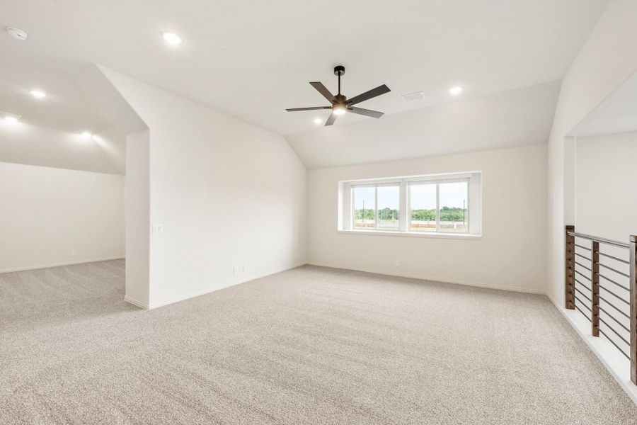 Open upstairs bonus room with carpet, ceiling fan, vaulted ceiling, and metal stair railing Open upstairs bonus room with carpet, ceiling fan, vaulted ceiling, and metal stair railing