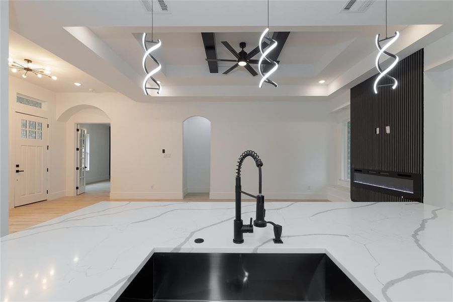 Kitchen featuring light stone countertops, a raised ceiling, open floor plan, light wood finished floors, and recessed lighting