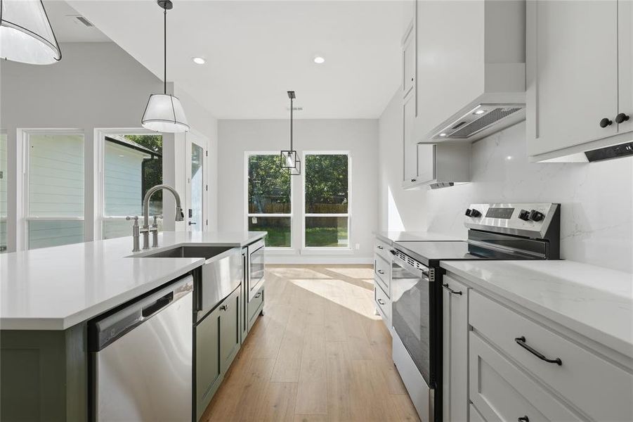 Spacious kitchen featuring an expansive island with a farmhouse sink, stainless steel appliances, light wood-finish flooring, and white countertops Spacious kitchen featuring an expansive island with a farmhouse sink, stainless steel appliances, light wood-finish flooring, and white countertops