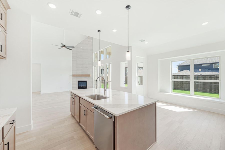 Open-concept kitchen with large island, quartz countertops, and vaulted ceiling overlooking living area with fireplace