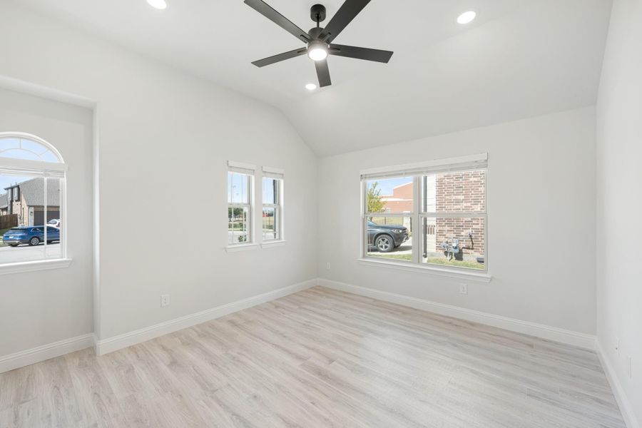 Empty bedroom with vaulted ceiling, black ceiling fan, light wood floors, and multiple windows