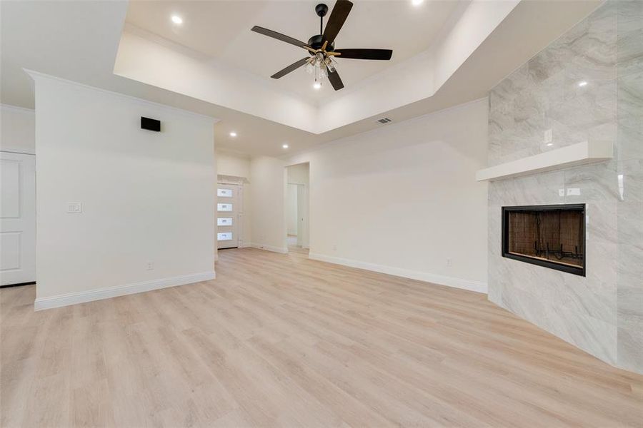 Unfurnished living room featuring light hardwood / wood-style flooring, a fireplace, a tray ceiling, and ceiling fan