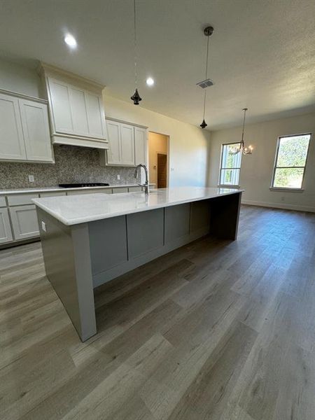 Kitchen featuring decorative backsplash, a large island, white cabinetry, light wood-type flooring, and hanging light fixtures