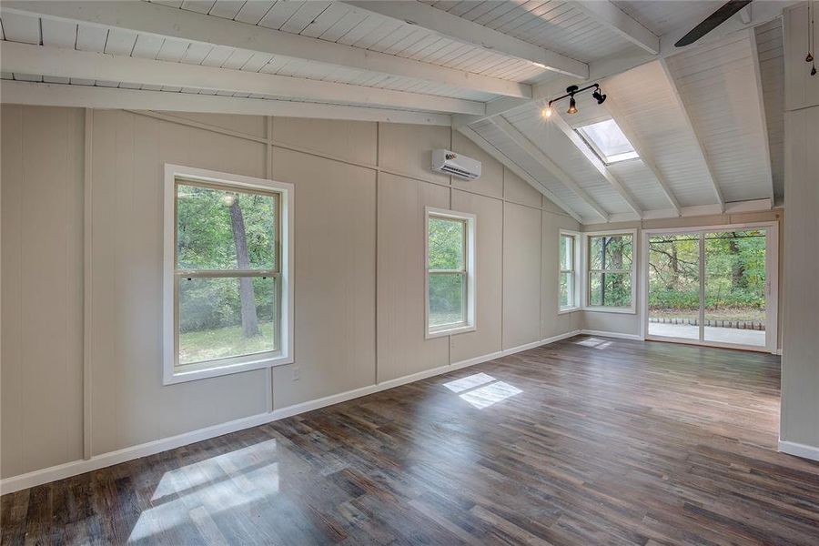 Empty room featuring track lighting, dark hardwood / wood-style flooring, an AC wall unit, and vaulted ceiling with skylight