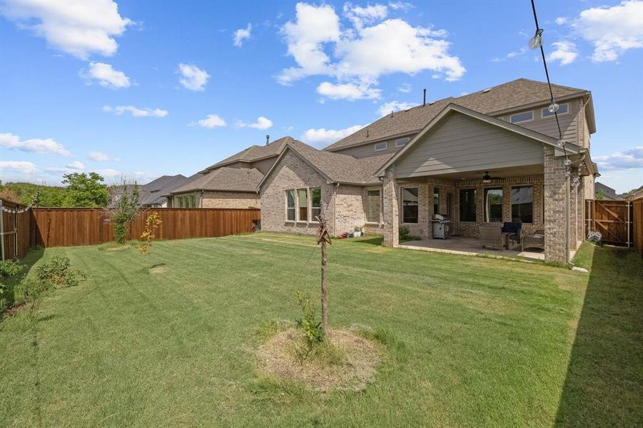 Rear view of property with a fenced backyard, brick siding, a ceiling fan, a yard, and a patio area