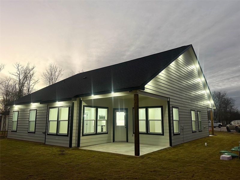 Rear view of house with a patio area, roof with shingles, and a yard