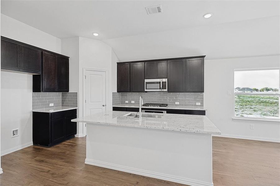 Kitchen featuring a center island with sink, hardwood / wood-style flooring, and tasteful backsplash