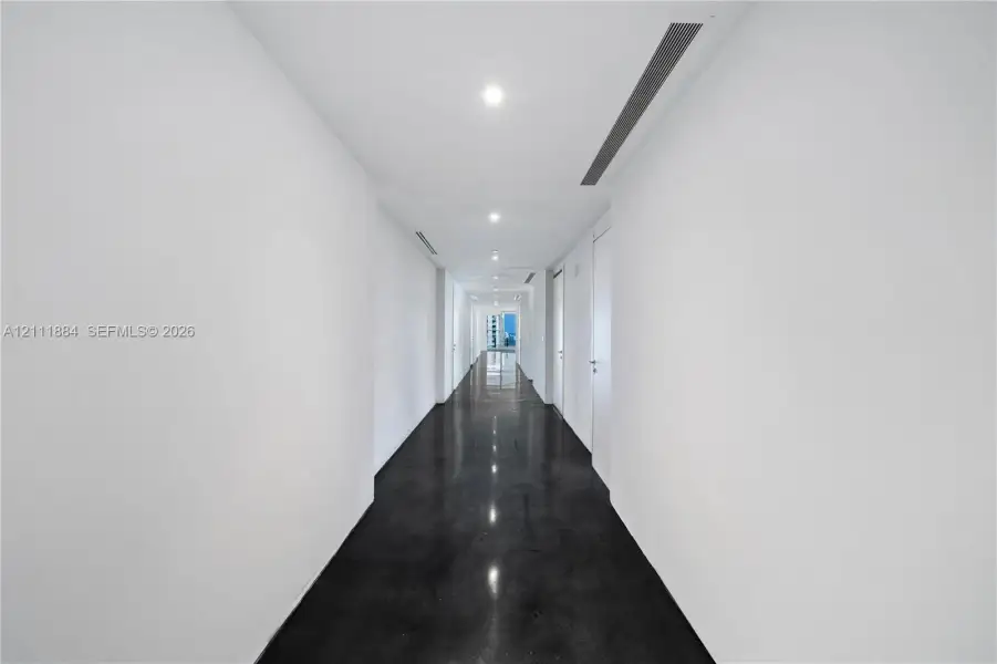 Hallway featuring high-gloss concrete flooring, recessed ceiling lighting, and crisp white wall finishes Hallway featuring high-gloss concrete flooring, recessed ceiling lighting, and crisp white wall finishes