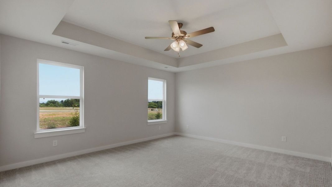 Large primary bedroom with windows and tray ceiling