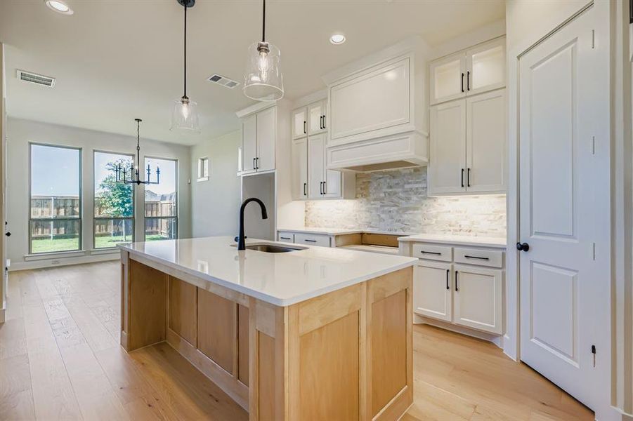 Kitchen with tasteful backsplash, white cabinetry, a center island with sink, light wood-style floors, and pendant lighting Kitchen with tasteful backsplash, white cabinetry, a center island with sink, light wood-style floors, and pendant lighting