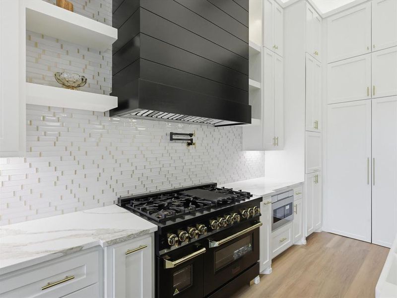 Gourmet kitchen featuring a large black range with gold-toned accents, a coordinating black range hood, and a white and gold-toned mosaic tile backsplash