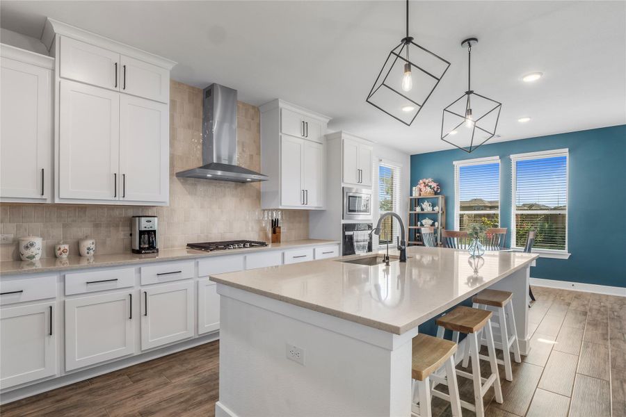 Kitchen with white cabinets, decorative backsplash, wall chimney range hood, a kitchen bar, and dark wood-style flooring Kitchen with white cabinets, decorative backsplash, wall chimney range hood, a kitchen bar, and dark wood-style flooring