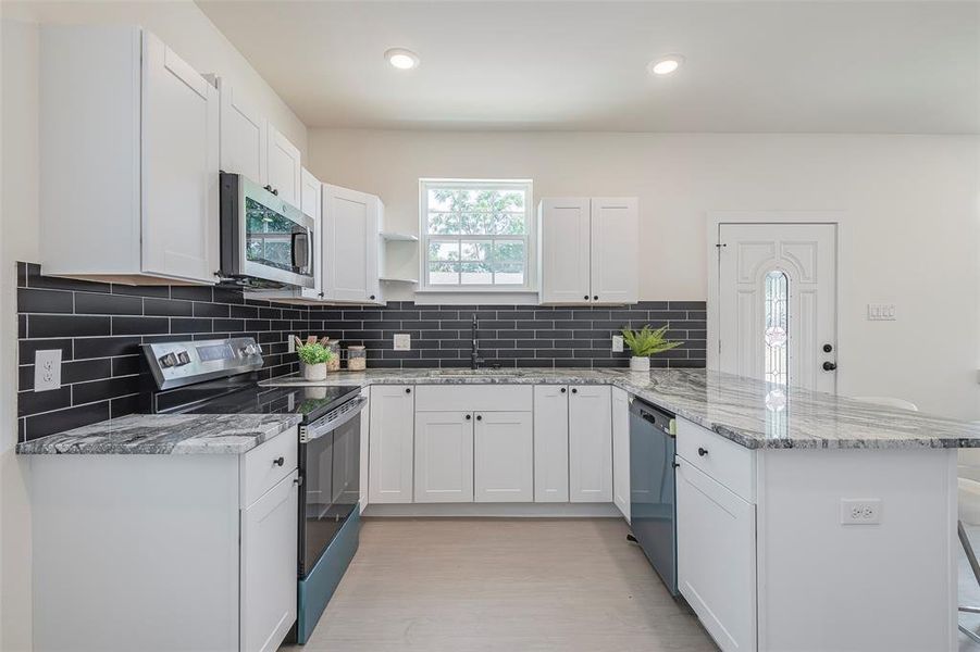 Kitchen featuring white cabinets, light stone countertops, stainless steel appliances, sink, and kitchen peninsula