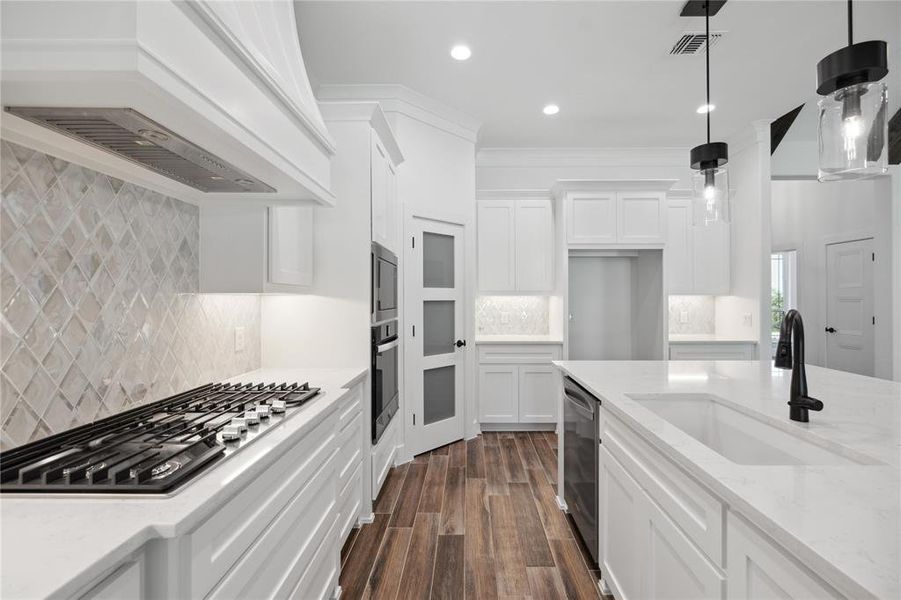 Kitchen with stainless steel appliances, sink, hanging light fixtures, backsplash, and custom range hood