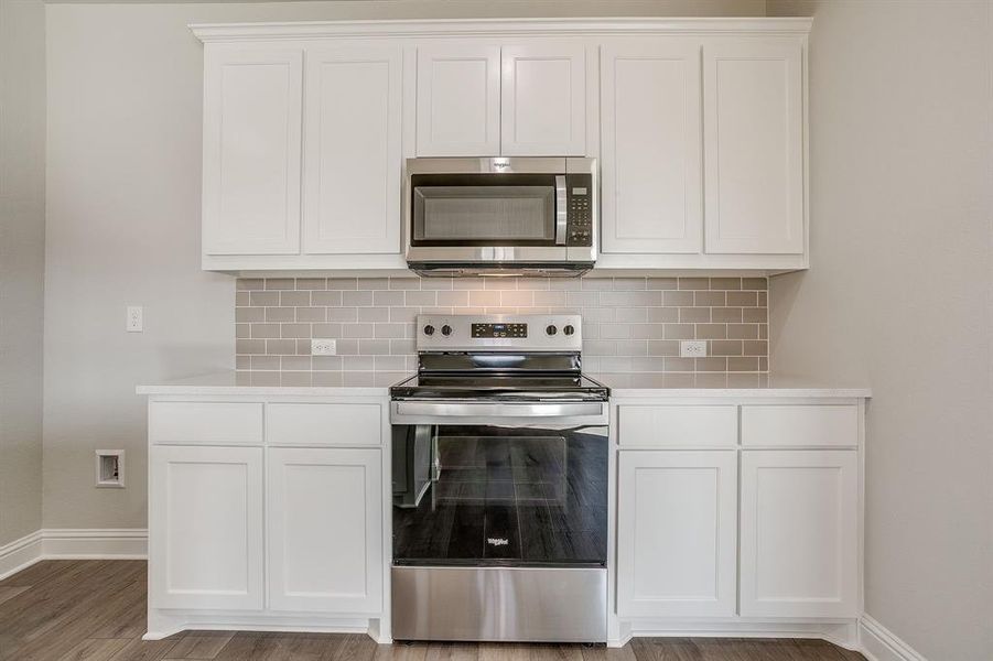 Kitchen with stainless steel appliances, white cabinetry, and decorative backsplash