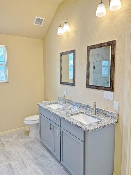 Full bathroom with double vanity, a textured wall, a marble finish shower, and vaulted ceiling
