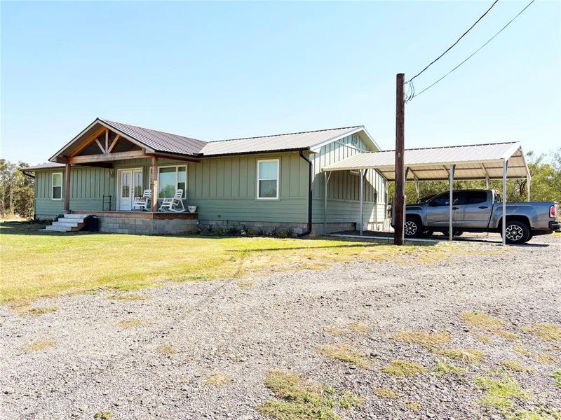 Side of home with covered porch, board and batten siding, a metal roof, a front lawn, and driveway Side of home with covered porch, board and batten siding, a metal roof, a front lawn, and driveway