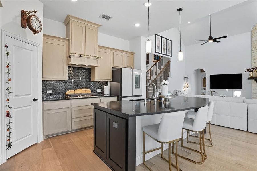 Kitchen featuring open floor plan, light wood-style flooring, tasteful backsplash, a breakfast bar, and a kitchen island with sink